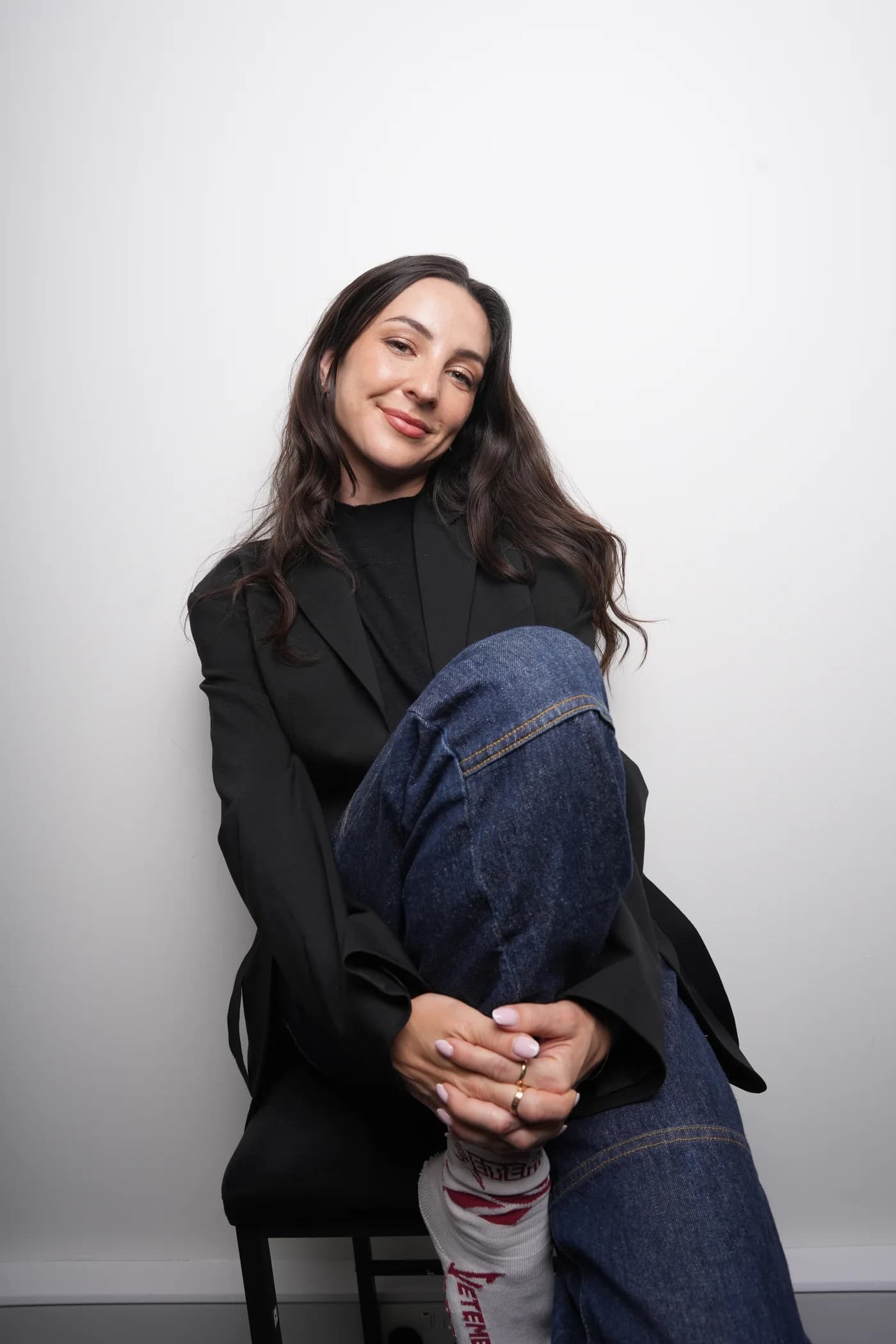 Anne-Sophie Fluri seated in a black blazer and blue jeans against a pale studio background
