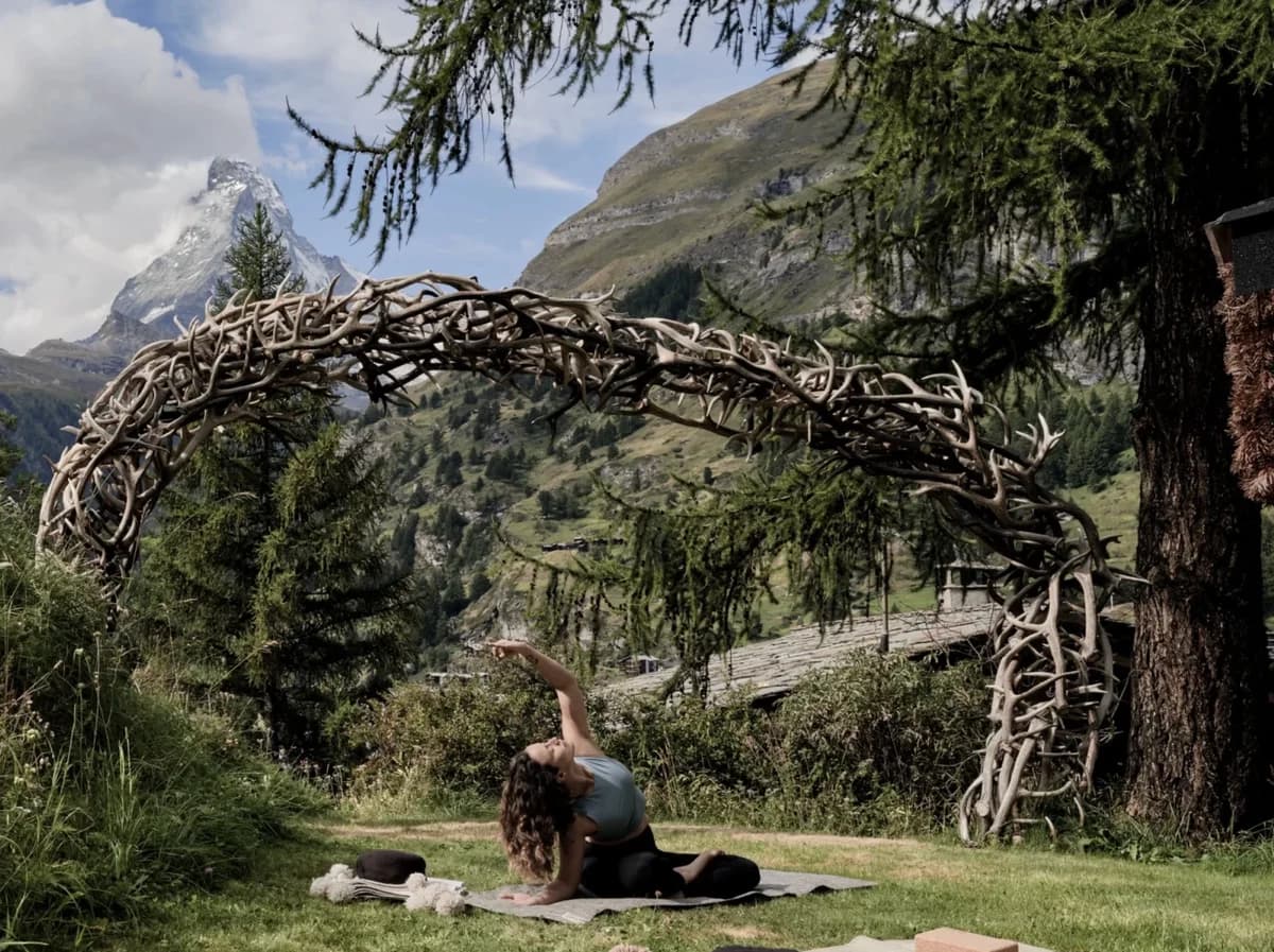 A seated outdoor yoga stretch beneath an antler arch at CERVO, with the Matterhorn beyond