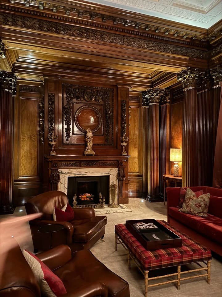 A wood-panelled lounge with red sofas and a fireplace, from Anne-Sophie’s Midnight in London carousel