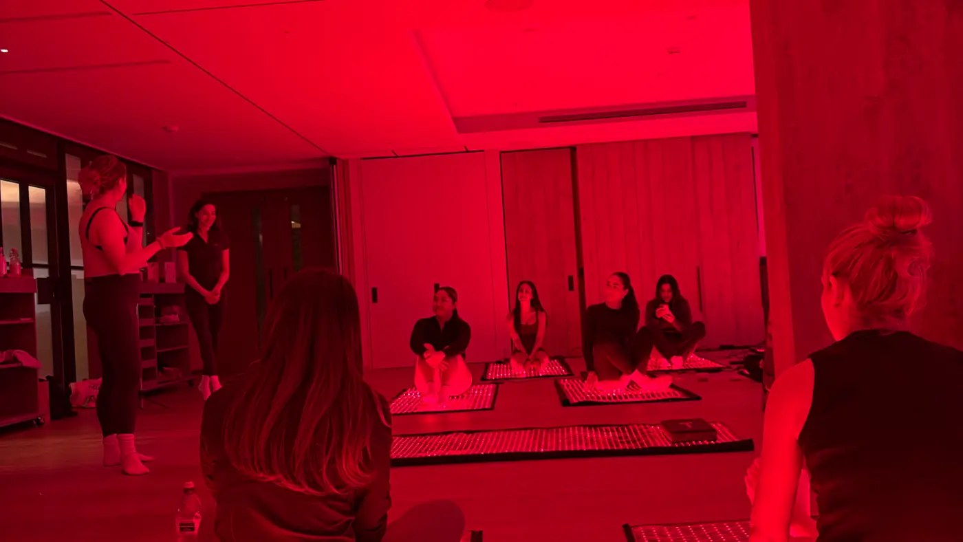 A session at 1 Hotel held under red light, guests sitting cross-legged on illuminated red-light panels while two speakers stand at the front